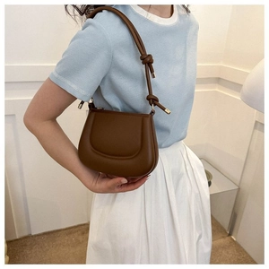 Détail d'un sac sous le bras en cuir marron avec des nœuds décoratifs sur la bandoulière