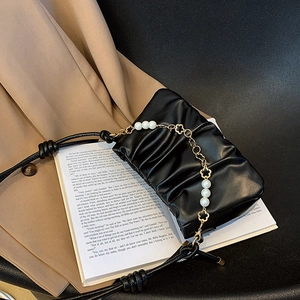Chic black pleated cloud bag with pearl floral chain on a beige blazer and book background