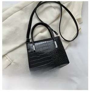 Dettaglio mini borsa nera a stampa coccodrillo con confronto dimensioni smartphone
