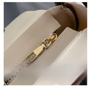 Close-up of golden zipper on off-white leather handbag with precise stitching detail