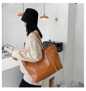 Detailed view of crocodile embossed caramel tote bag worn on shoulder in a cafe setting