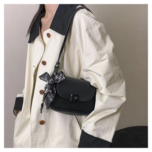 Detail of black leather crossbody bag with decorative scarf on a stylish trench coat