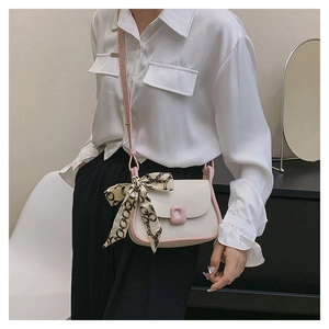 Detail of off-white crossbody bag with pink trim and silk scarf on a white shirt