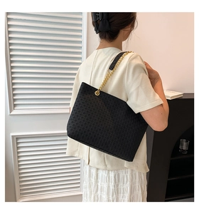 Detalle del bolso tote negro con textura tejida y correa de cadena dorada elegante