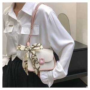 Detail of white leather shoulder bag with pink trim and decorative silk scarf strap