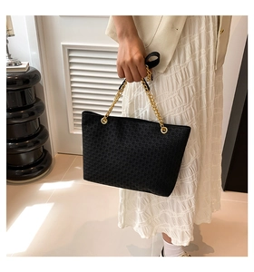Detalle de bolso tote negro con textura de rejilla en relieve y cadena dorada