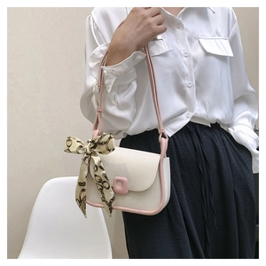 Close-up of a white leather flap bag with pink edges and decorative silk scarf strap