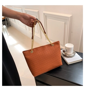Detalle del bolso tote naranja con textura tejida y correa de cadena dorada