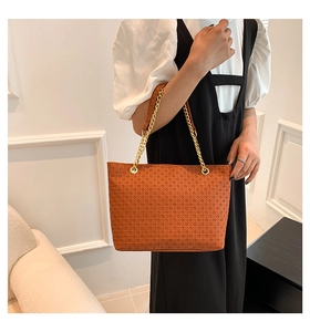 Detalle del bolso tote marrón con relieve trenzado y correa de cadena dorada
