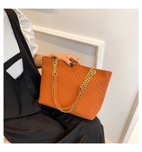 Detalle del bolso tote trenzado marrón naranja con cadena dorada y superficie texturizada