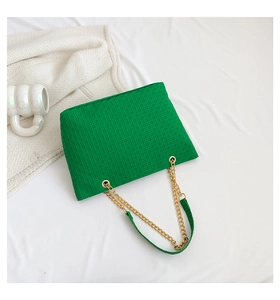 Detalle del bolso tote trenzado verde con cadena de metal dorado y textura única