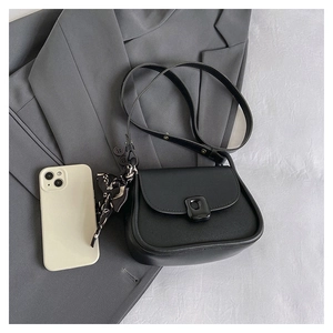 Detail of black mini square bag with decorative silk scarf on a grey suit background