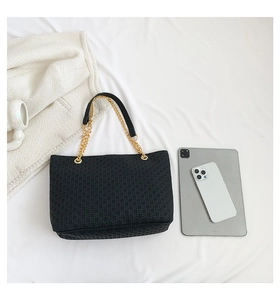 Vista superior de bolso tote tejido negro con cadenas doradas junto a una tableta