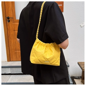 Detailed back view of a bright yellow quilted shoulder bag with chain strap on a model