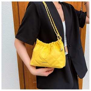 Detail of quilted bright yellow leather shoulder bag with gold chain and ball charm