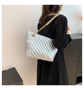 Détail d'un sac cabas argenté matelassé avec chaîne dorée porté par un mannequin