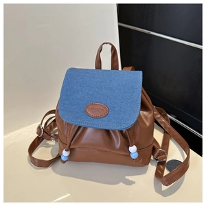 Detail eines Mini-Rucksacks aus braunem Leder und blauem Denim mit Kordelzug und Label