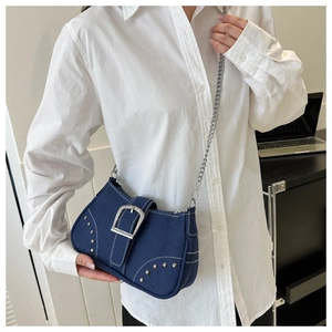 Close-up of blue denim underarm bag with silver studs and metal chain on a model