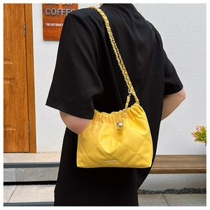 Detail of a bright yellow quilted shoulder bag with chain strap and gold sphere charm