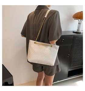 Detalle de bolso tote blanco trenzado con cadena dorada y acabado de cuero texturizado