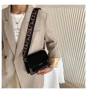Detail of a black crossbody bag with decorative wide jacquard strap on beige blazer