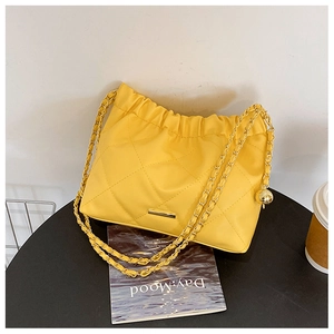 Detail of yellow quilted chain bag featuring elegant ruched top and golden ball pendant