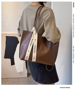 Detail of dark brown leather tote bag with a decorative fashion logo woven strap