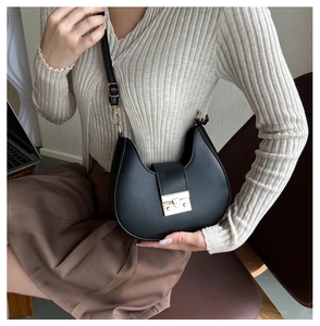 Detail of a black leather crescent shoulder bag with gold clasp and adjustable strap