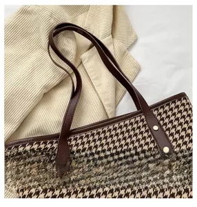 Detail of plaid tote bag featuring leather handles and brand emblem on corduroy background