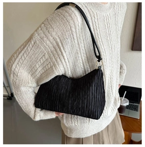 Sac baguette plissé noir avec boucles dorées porté par un mannequin dans un décor chaleureux