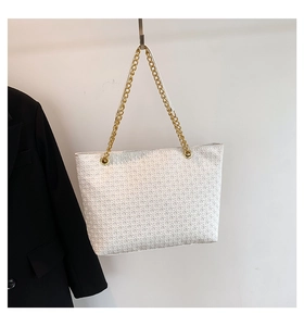Detalle del bolso tote blanco trenzado con correa de cadena dorada y textura geométrica