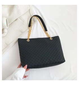 Detalle del bolso tote negro tejido con cadena dorada sobre fondo de tela blanca