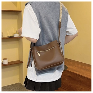 Detail of dark brown matte leather crossbody bag with geometric woven strap on shoulder