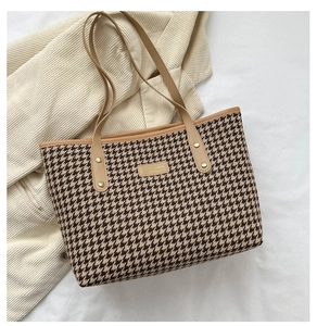Detail of houndstooth tote bag with brown leather handles on soft neutral fabric