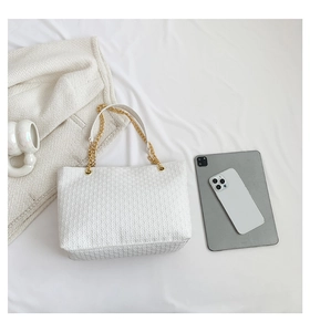 Detalle de bolso tote tejido con correa de cadena y varios accesorios de escritorio