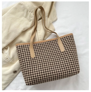 Detail of classic houndstooth tote bag with brown leather handles on soft beige fabric