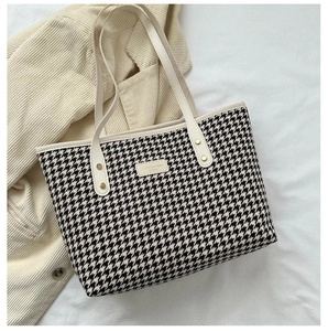 Detail of houndstooth fabric tote bag with cream leather handles and gold metal hardware