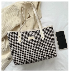 Detail of houndstooth tote bag with cream leather handle and golden metal logo plate