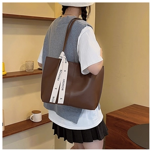 Close-up of matte brown tote bag with decorative fashion ribbon and vertical stitching