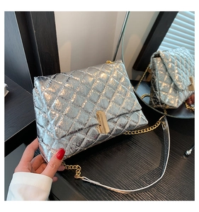 Detailed view of silver quilted crossbody bag with gold twist lock on wooden surface