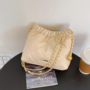Quilted cream crossbody bag with gold chain strap and drawstring design on black table