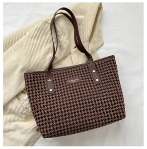 Close-up of houndstooth tote bag texture with leather brand logo and gold rivets