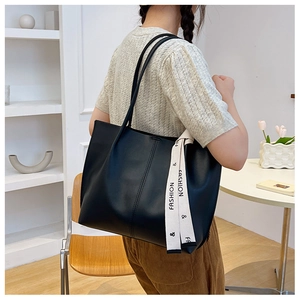 Detail of black faux leather tote bag featuring a decorative fashion ribbon strap