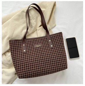 Macro detail of houndstooth tote bag showing leather handles and metallic rivets