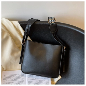 Minimalist black matte leather bucket bag with geometric wide strap on a modern chair