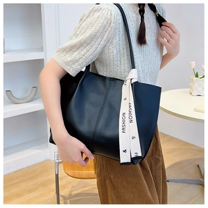 Close-up of black leather tote bag featuring a decorative fashion letter ribbon