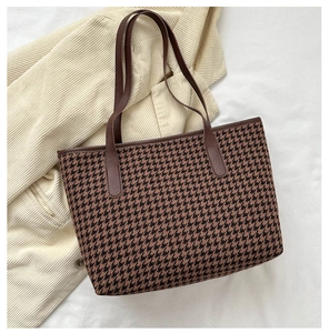 Detail of large houndstooth tote bag with brown leather straps on a corduroy background