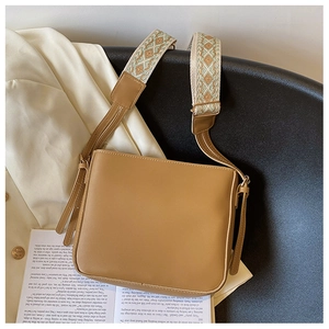 Close-up of camel PU leather crossbody bag with geometric jacquard wide strap on a chair