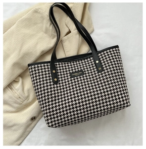 Detail shot of black and white houndstooth tote bag with leather straps and gold rivets