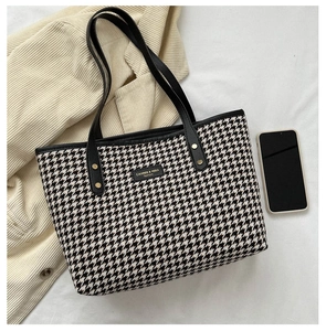 Close-up of houndstooth tote bag with black leather strap and gold-lettered logo detail